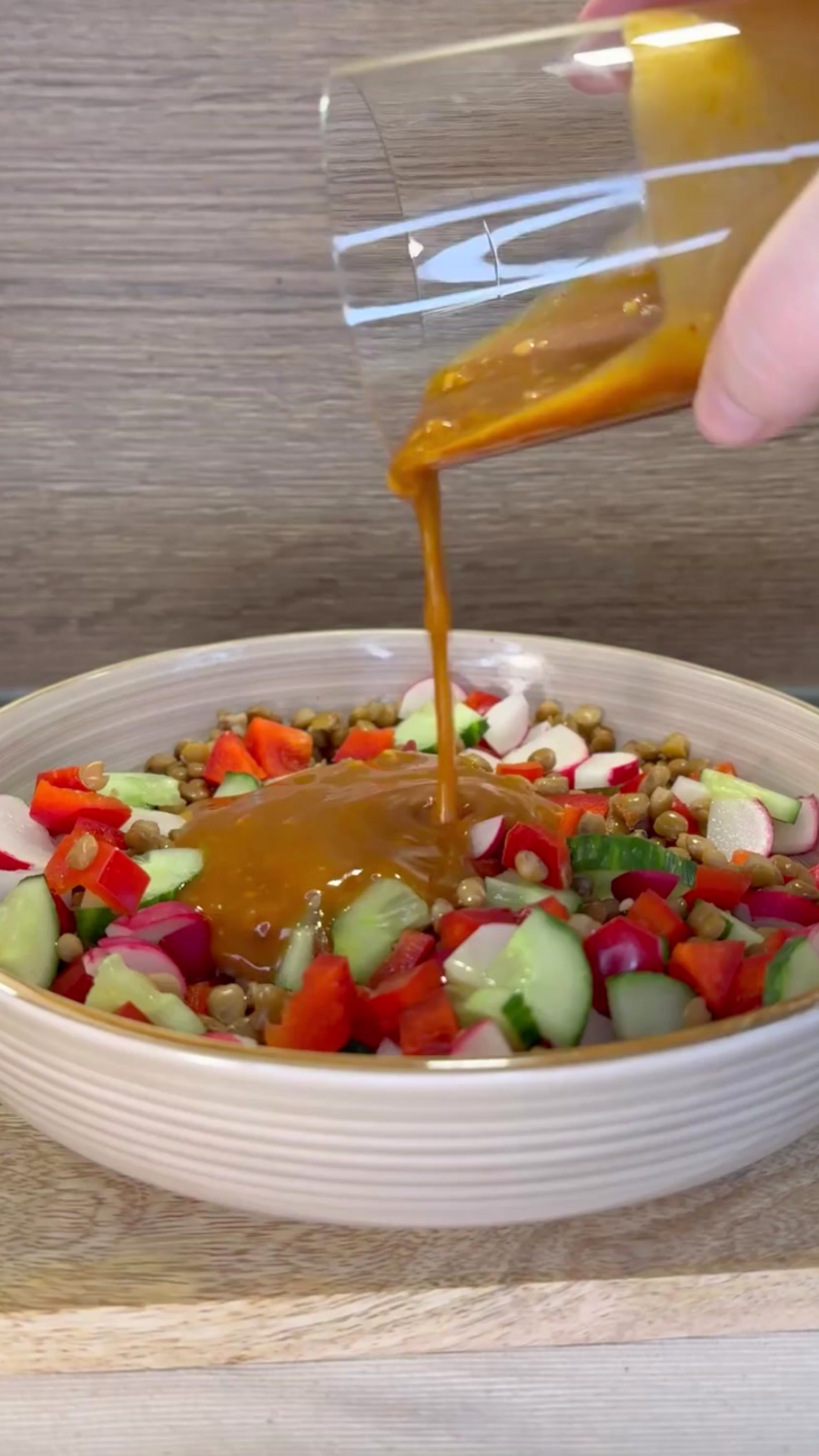 Hand gießt Dressing über bunten Linsensalat mit Gurke, Radieschen und Paprika