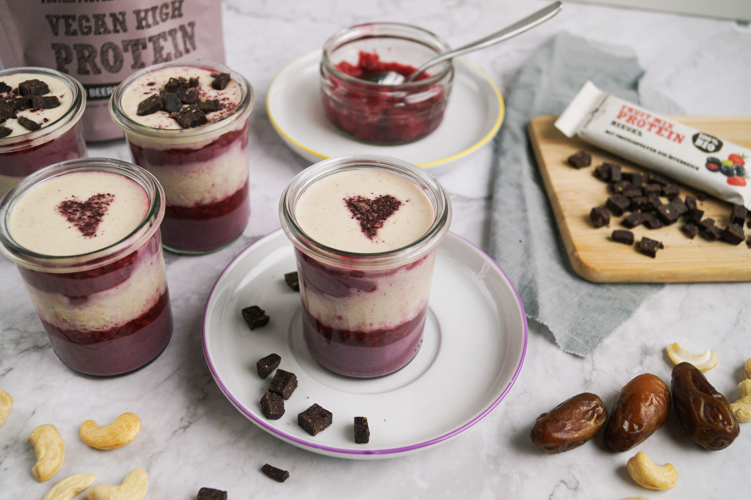Veganes Schichtdessert im Glas mit Beeren, Vanillecreme und Aronia-Herz, dazu Schalk Mühle Vegan High Protein