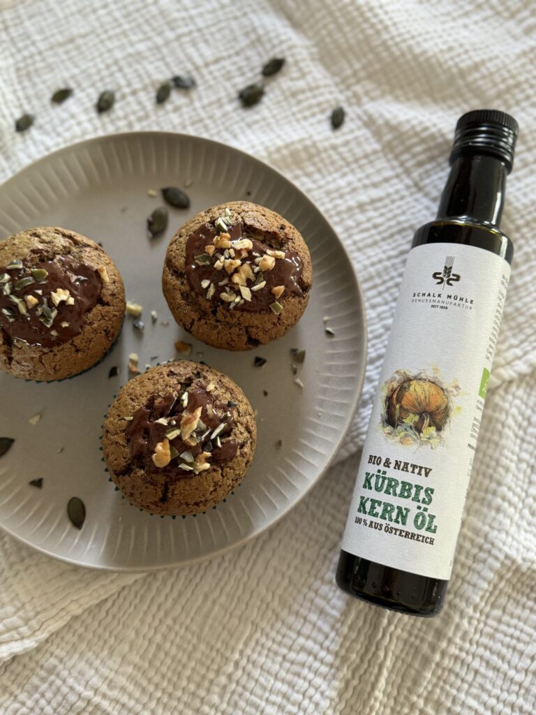 Schoko-Muffins mit Kürbiskernen und Walnüssen auf Teller, daneben Schalk Mühle Kürbiskernöl