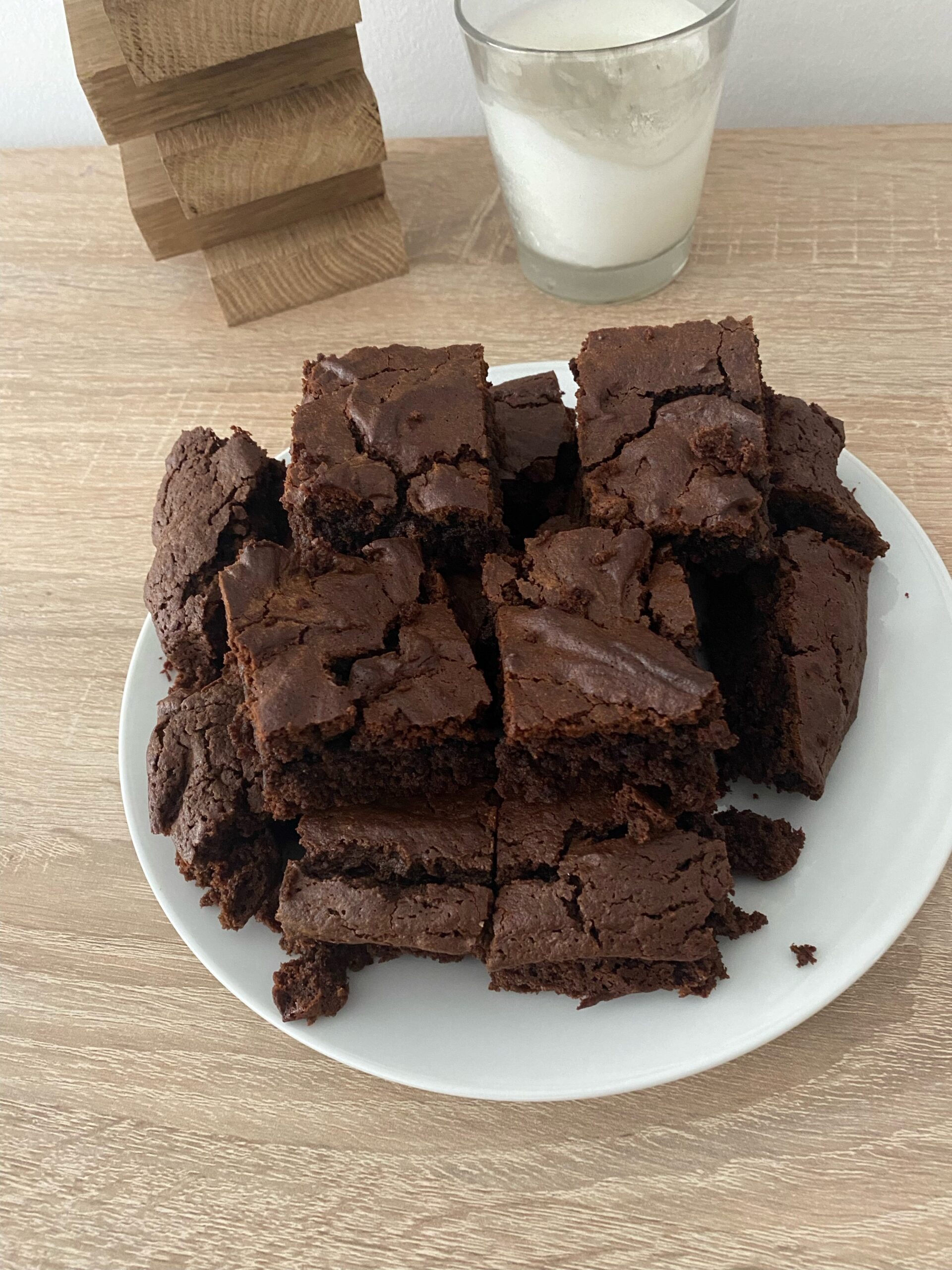 Gestapelte Schokobrownies auf einem weißen Teller, dahinter ein Glas Milch