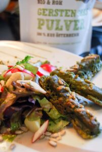 Grüne Tofu-Sticks auf Blattsalat mit Radieschen und Sonnenblumenkernen, dahinter Gerstenpulver