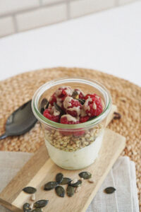Topfencreme im Glas mit Buchweizen, Himbeeren, Nussmus und Kürbiskernen