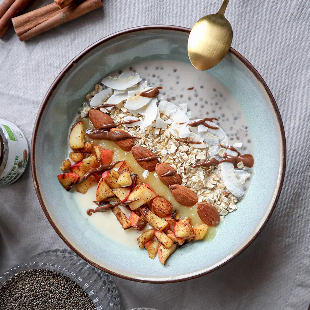 Frühstücksschale mit Haferflocken, Kokoschips, Mandeln, gebratenen Apfelstücken und Chiasamen