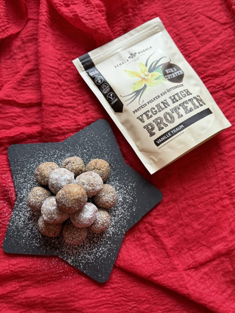 Vanille-Kugeln mit Staubzucker auf Schieferstern, daneben Schalk Mühle Vegan High Protein Vanille
