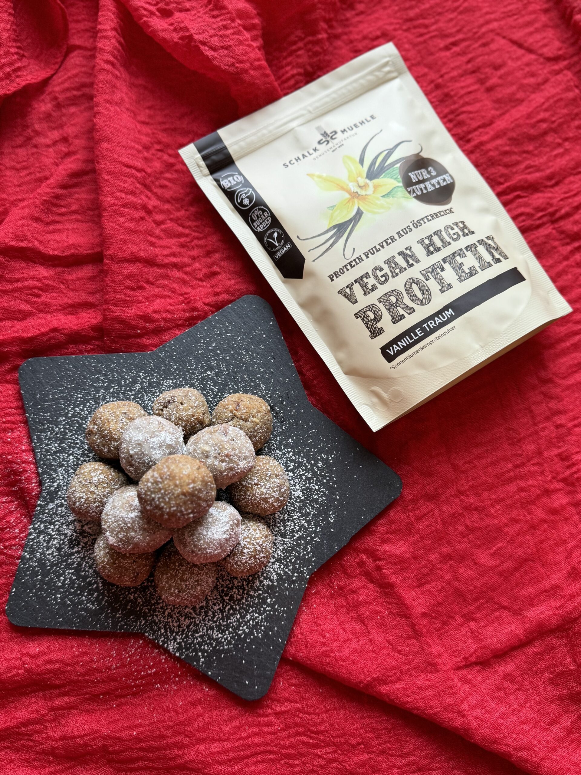 Vanille-Kugeln mit Staubzucker auf Schieferstern, daneben Schalk Mühle Vegan High Protein Vanille