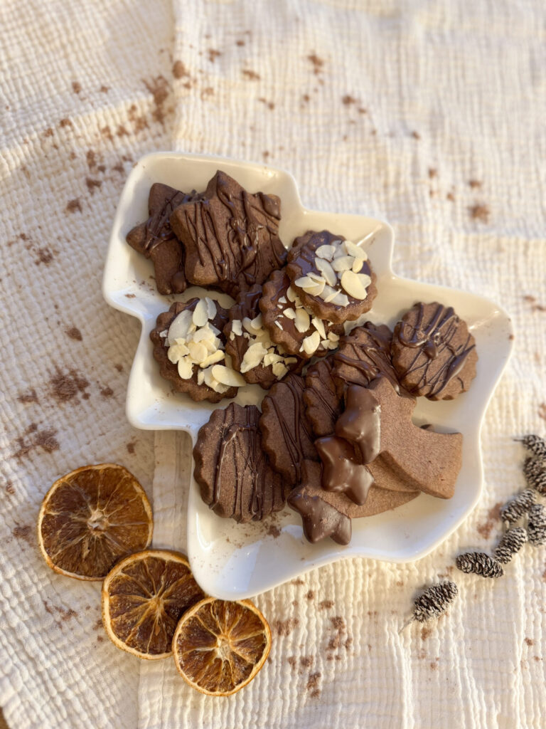 Schoko-Mürbteigkekse in Weihnachtsformen mit Schokoglasur und Mandeln, daneben getrocknete Orangenscheiben
