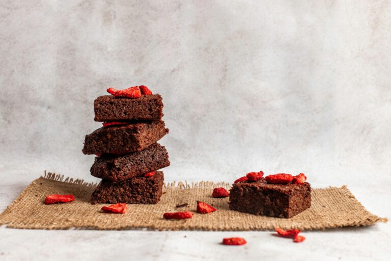 Gestapelte vegane Schoko-Brownies mit gefriergetrockneten Erdbeerstücken auf Jutestoff vor hellem Hintergrund
