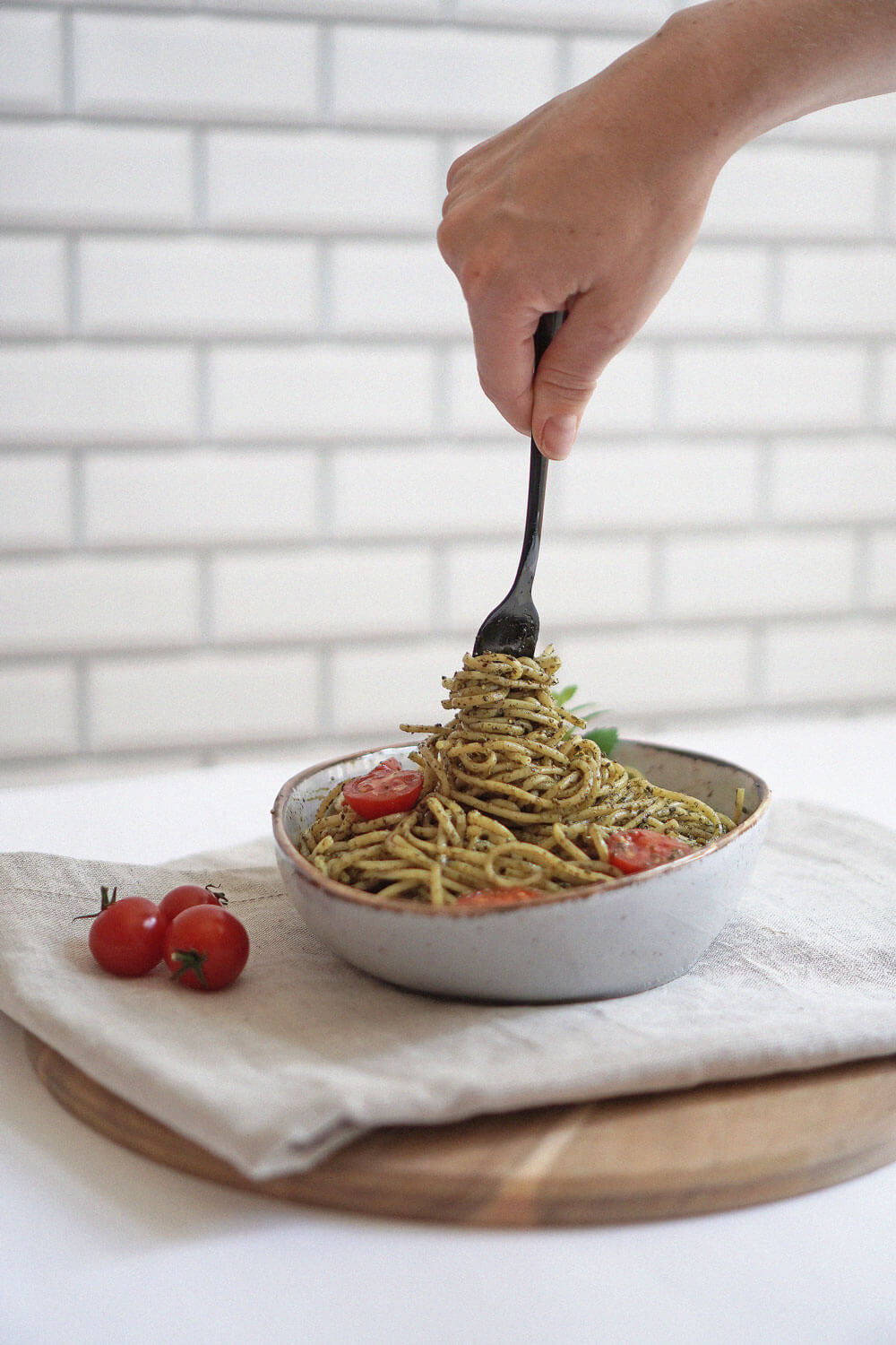 Vollkorn-Spaghetti mit Pesto und Kirschtomaten, eine Gabel hebt eine Portion aus der Schüssel