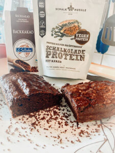 Schoko-Brownies mit Glasur, dahinter Backkakao und Schalk Mühle Schalkolade-Protein