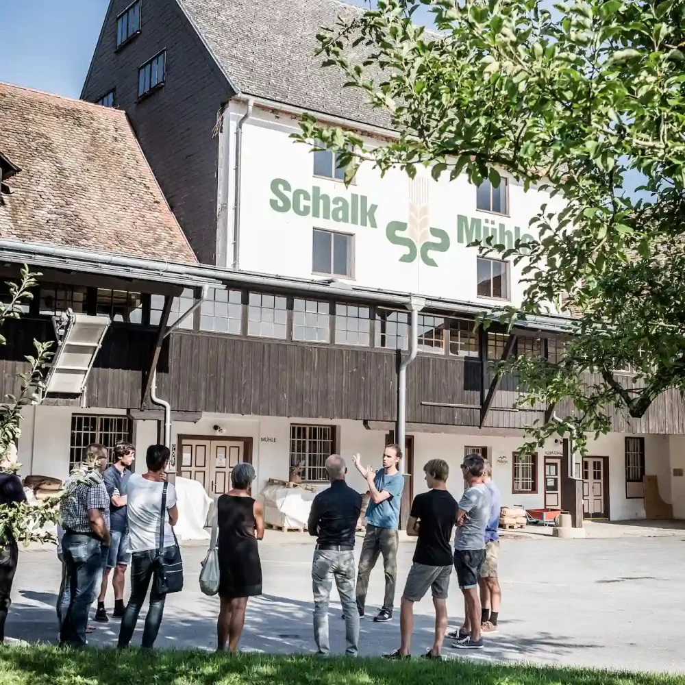 Außenansicht der Schalk Mühle mit Schriftzug am Gebäude und Besuchergruppe bei einer Führung im Hof