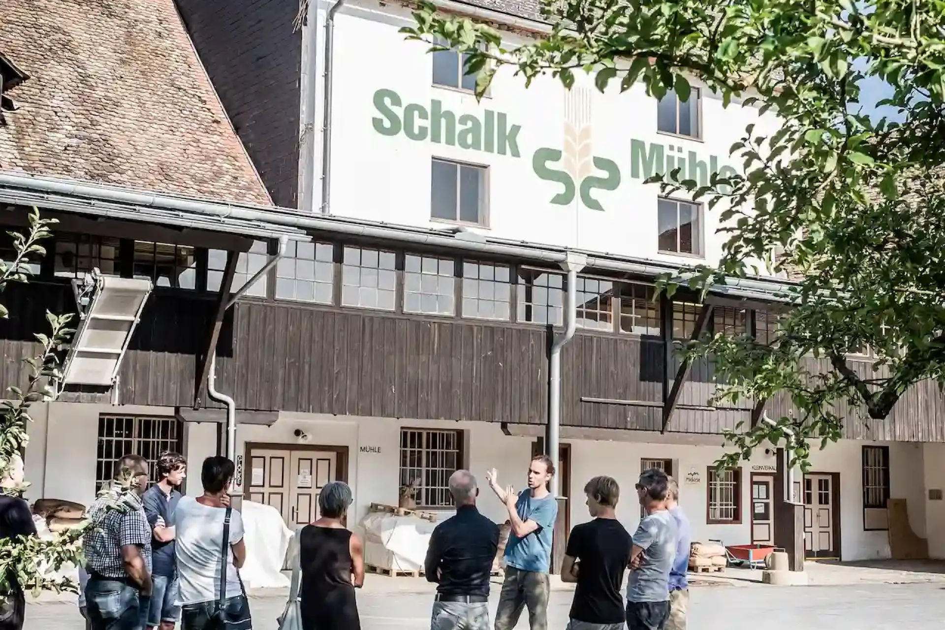 Außenansicht der Schalk Mühle mit Schriftzug am Gebäude und Besuchergruppe bei einer Führung im Hof