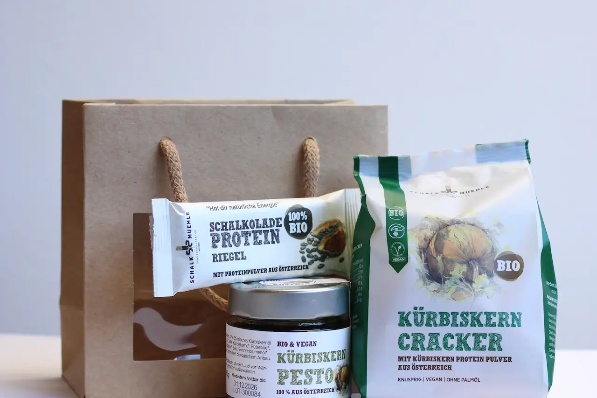 Kraft paper bag with pumpkin seed crackers, pumpkin seed pesto in a jar, and protein bar