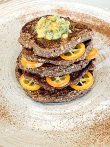 Stapel dunkler Buchweizen-Pancakes mit Kumquat-Scheiben und Fruchttopping auf einem Teller