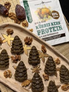 Grüne Kürbiskern-Kekse in Tannenbaumform mit Walnüssen und Datteln neben Schalk Mühle Kürbis Kern Protein