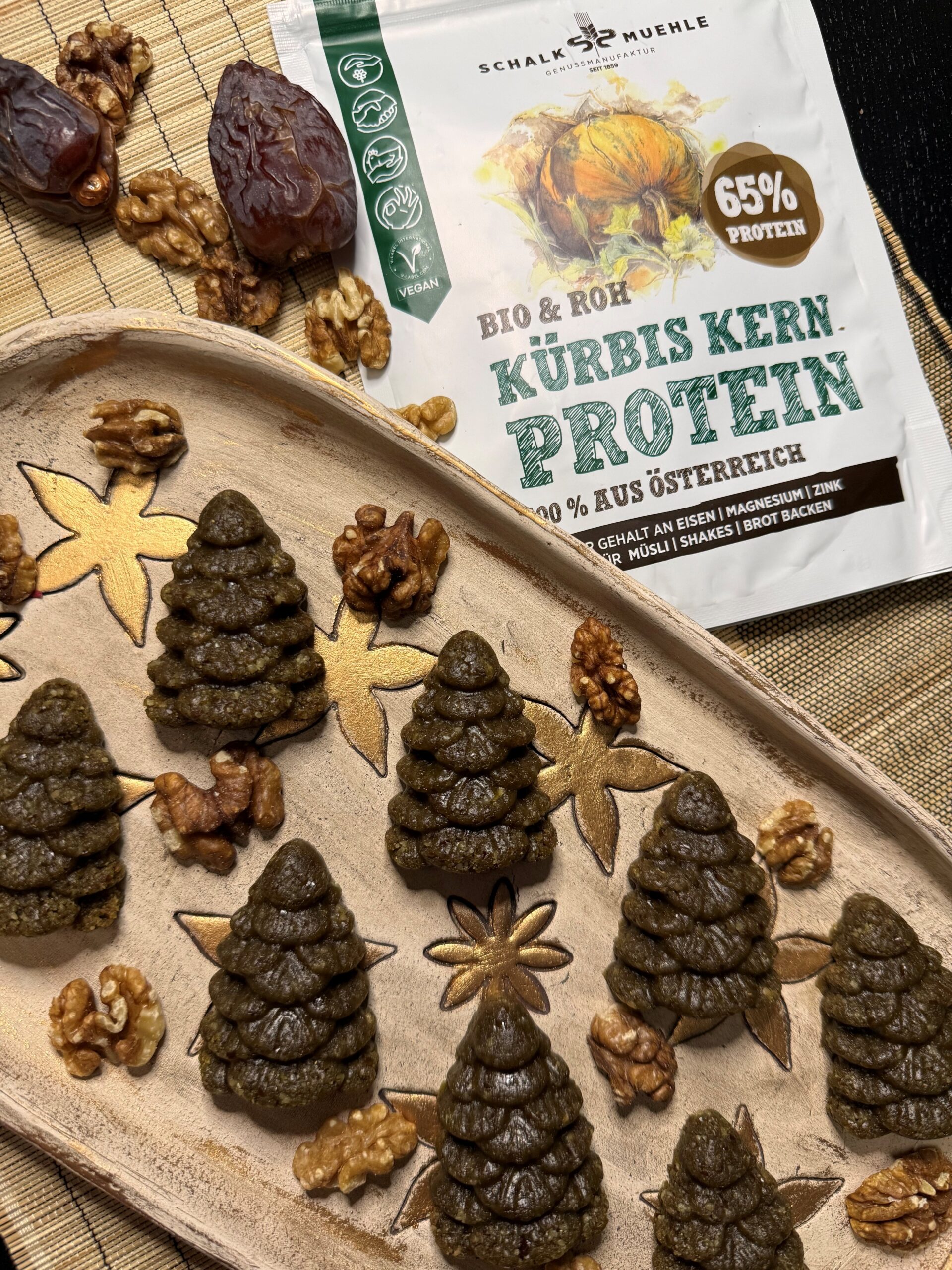 Grüne Kürbiskern-Kekse in Tannenbaumform mit Walnüssen und Datteln neben Schalk Mühle Kürbis Kern Protein