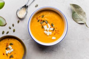 Cremige Kürbissuppe in zwei Schalen, garniert mit Kürbiskernen, Fetawürfeln und Paprikapulver