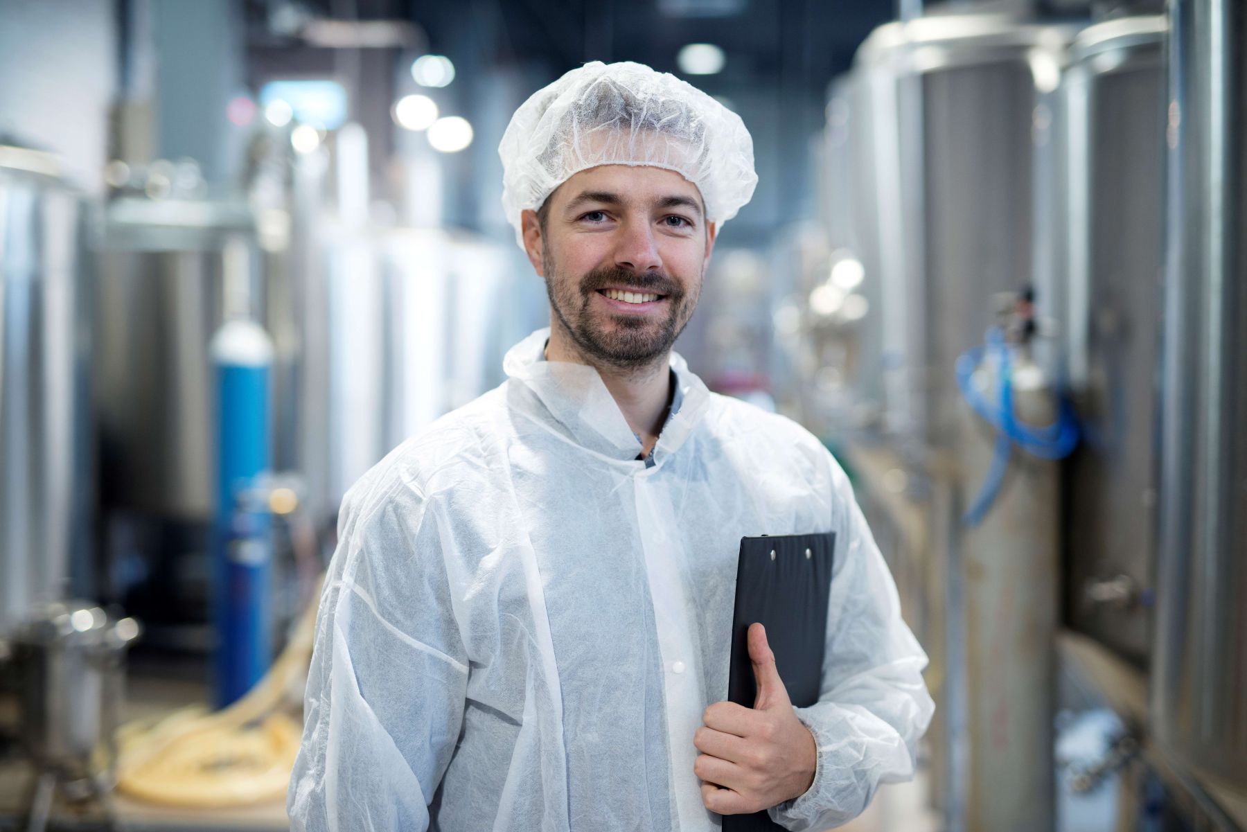 Protrait eines Mannes mit Haarnetz und weißem Kittel in einer Produktion, lächelnd