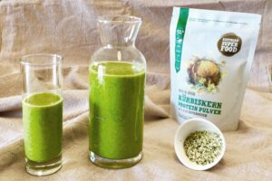 Grüner Smoothie in Karaffe und Glas mit Kürbiskern-Proteinpulver und Hanfsamen