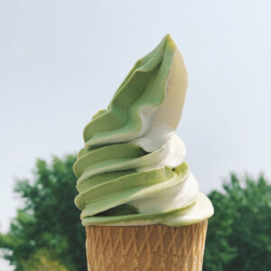 Matcha-Vanille-Softeis im Waffelbecher vor grünem Baumhintergrund